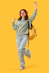 Female Indian student in headphones with backpack dancing on yellow background