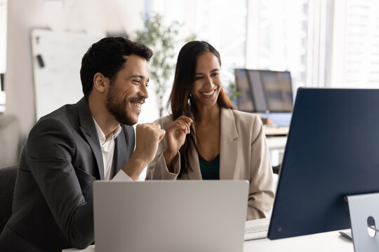 Two diverse colleagues engaged in collaborative meeting in office, looking at computer monitor, discussing ideas and sharing insights, laughing during teamwork, communication, and professional synergy