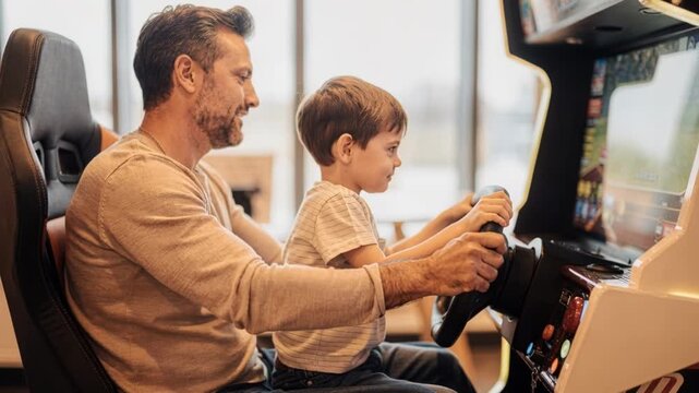 Joyful father son bonding through arcade racing game. Child smiles during family fun activity within local entertainment center using steering wheel
