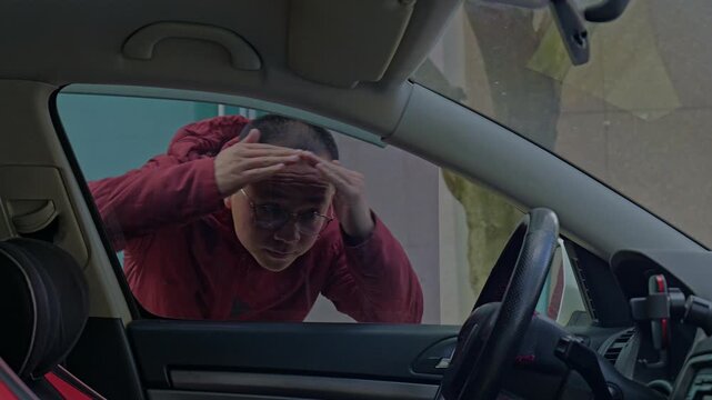 A guy peers inside through the car window, blocked by tint.
