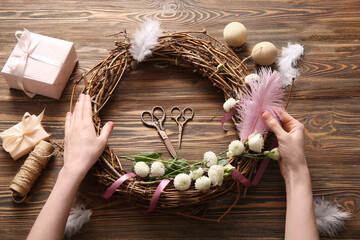 Woman making Easter wreath with eggs, feathers and flowers on brown wooden background © Pixel-Shot