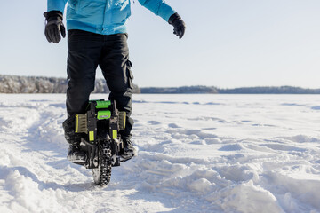 Person riding electric unicycle monowheel on frozen snow-covered lake field in winter landscape with blue sky forest background, extreme outdoor adventure sport activity © MarijaBazarova