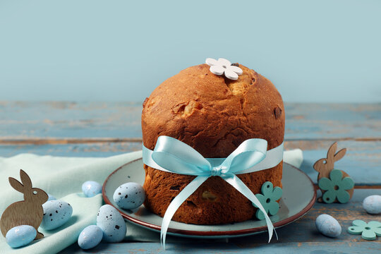 Plate with delicious Easter cake, painted eggs and bunnies on blue wooden table