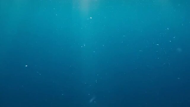Deep blue underwater scene with floating particles and sun rays.
