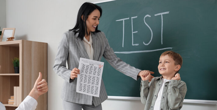 Happy schoolboy and teacher with results of test in classroom