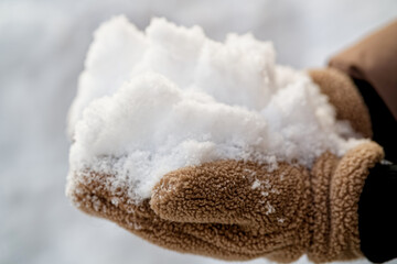 Close up of fluffy brown gloves holding a large handful of ice crystals. Person playing outside in the cold season. Symbol of heavy precipitation and frost. Photo © slexp880