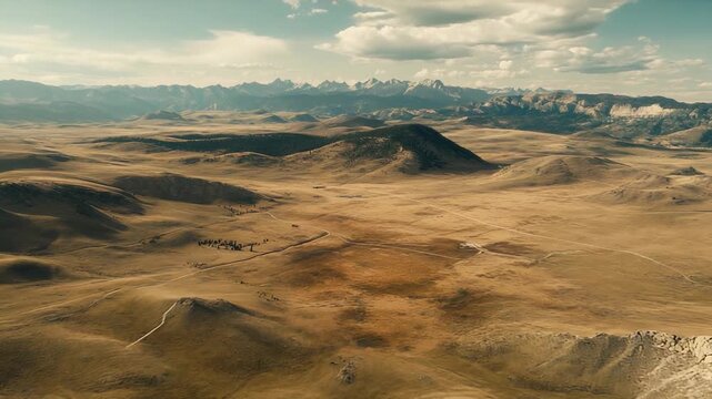 Expansive prairie and rolling hills stretch toward a rugged mountain range under a dramatic cloudscape, sunlit textures and sparse vegetation conveying serene, remote beauty