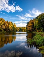 Autumnal trees surround a serene lake reflecting the sky with wispy clouds. Vegetation lines the shore