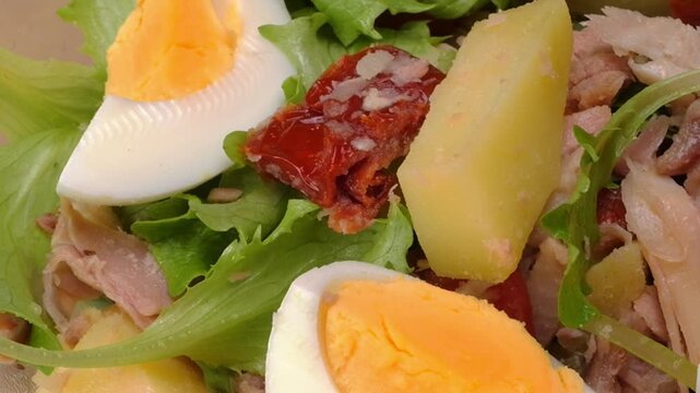 Primo piano di ciotola con insalata di lattuga, uovo, pomodori, olive, patate, tonno e capperi