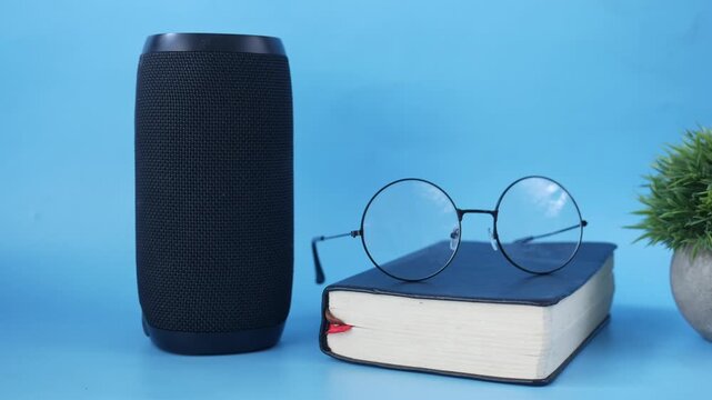 Smart speaker with glasses and book on blue background in motion