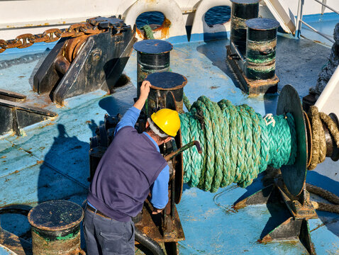 Worker with safety helmet operating winch with green rope on board a vessel