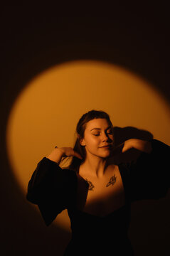Moody warm portrait of woman in black dress with chest tattoos under circular spotlight for poster and editorial background design