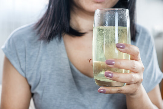 Close-up of a woman holding a glass with a dissolving effervescent antacid tablet. Bubbles rise in water for heartburn relief, indigestion treatment, and stomach healthcare concept at home