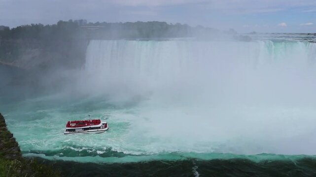 
Niagara Falls - Edge of Horseshoe Falls - blue water flows over the edge of the cliff, a cruise ship with tourists came close to the falling water, entertainment in Niagara Falls, Ontario, Canada.