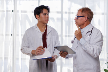 Two male doctors stand together, one holding a clipboard and the other a tablet, in a modern...