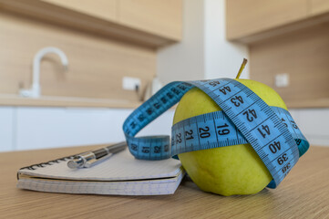 A ripe green apple wrapped in a measuring tape lies on the table, a diet menu