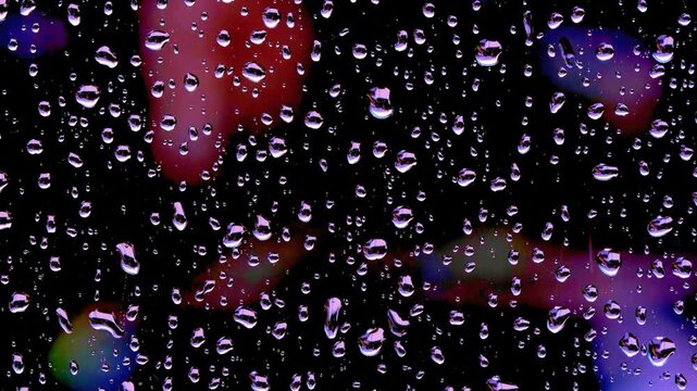 Raindrops falling and sliding down a window pane at night with moody purple ambient lighting.