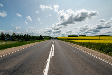 Scenic summer landscape with yellow rapeseed field under blue cloudy sky