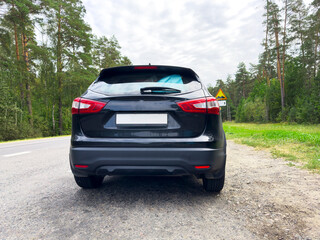 Black car parked on rural road with forest background. Rear view vehicle stands on countryside asphalt. Transport scene for travel, automotive, mobility concept..