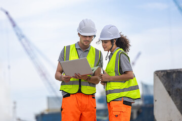 Technical team of logistics managers coordinating operations using a digital tablet at port terminal, engineers using laptop to review project data at construction site with cranes in the background