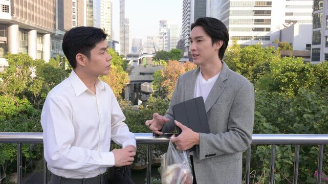 Two asian businessmen talking on a city skywalk