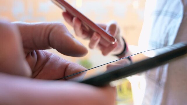 Close-up video showing the hands of two people facing each other while using smartphones. The scene captures modern social interaction, digital communication, and everyday mobile technology use