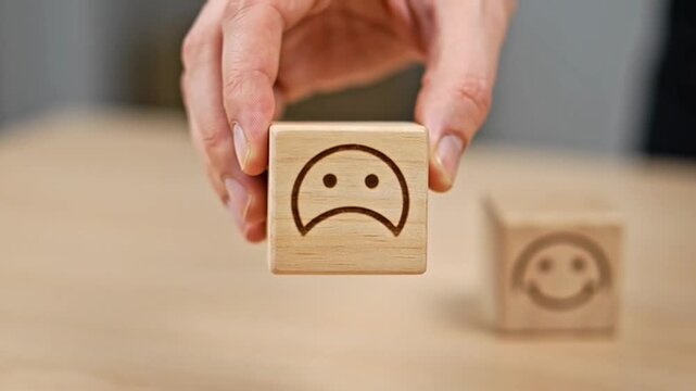 Hand choosing between happy and sad face blocks on wooden table