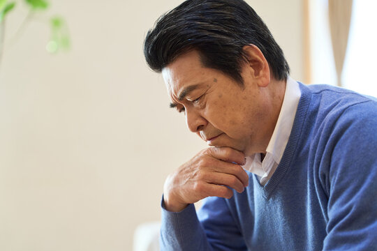 部屋で悩むアジア人シニア男性
