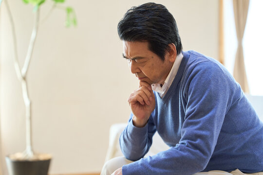 部屋で悩むアジア人シニア男性
