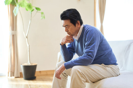 部屋で悩むアジア人シニア男性