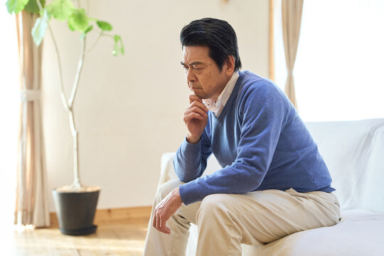 部屋で悩むアジア人シニア男性