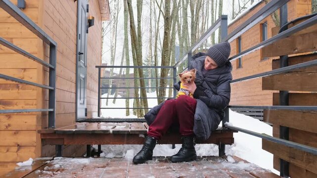 Woman sitting on porch of country house with dog, enjoying quiet winter moment without devices. Digital detox, offline lifestyle and mindful break from technology.
