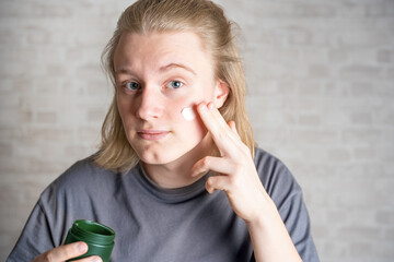 Fototapeta na wymiar Young man (zoomer, teenager) applying moisturizer on his face