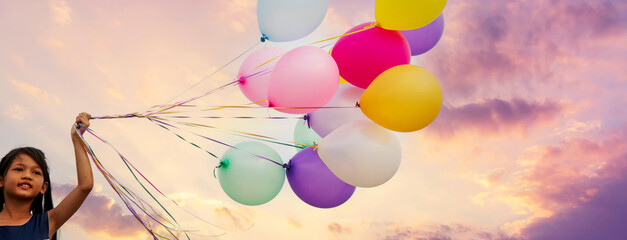 Banner Cheerful cute girl holding balloons run green meadow violet purple pastel sky happiness. Banner Hands holding vibrant air balloons birthday party happy times summer pueple sky with copy space