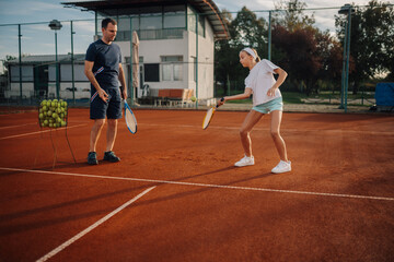 Obraz premium Father coaching daughter on clay tennis court