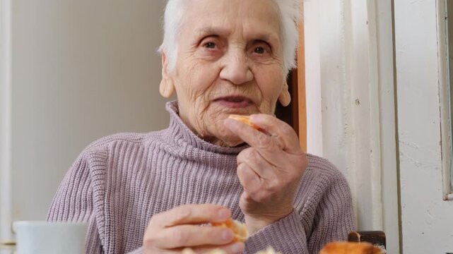 Kind smiling senior woman eats mandarin slice while talking. Gray haired elderly woman putting mandarin or orange segment into mouth. healthy active seniors and proper nutrition in retirement.
