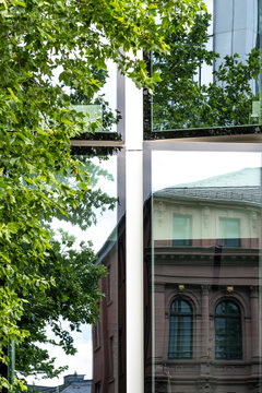 Urban architecture in Frankfurt with trees framing a cross monument in daylight as modern and historic facade elements meet in city contrast
