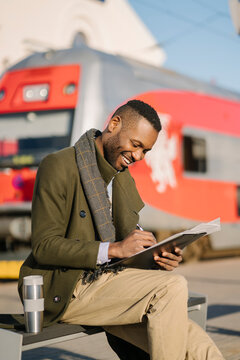 Portrait of stylish businessman with reusable cup and documents waiting for the train