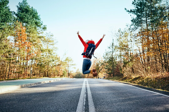 Cheerful woman jumping on an empty road during backpacking trip