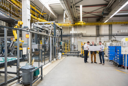 Three men with blueprint talking in factory shop floor