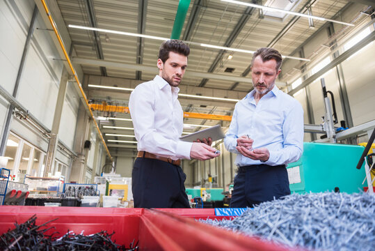 Two businessmen with tablet in factory standing at containers with shred