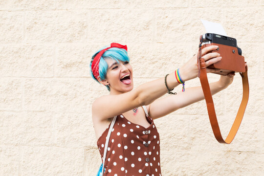 Portrait of young woman with blue dyed hair taking selfie with instant camera
