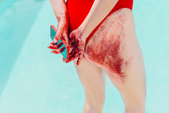 Rear view of woman holding cell phone with bottom covered with red sand
