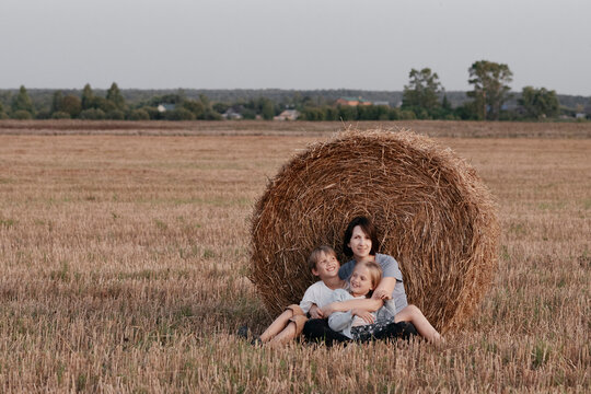Woman with two kids sitting near a haystack on a stubble field