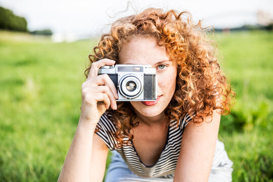 Young woman on a meadow taking picture of viewer with camera