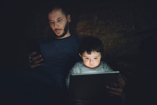 Father and daughter using phablet and digital tablet at home in the dark