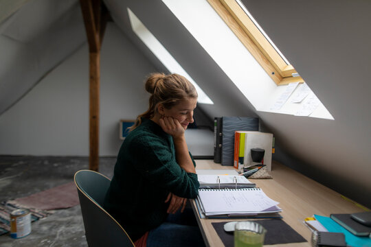 Young woman sitting at desk in attic studying folder
