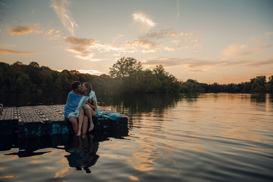 Young couple sitting on bathing platform, kissing, wrapped in towel