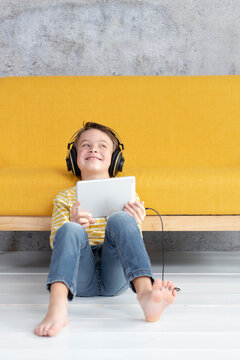 Boy playing with tablet and wearing headphones at a yellow couch