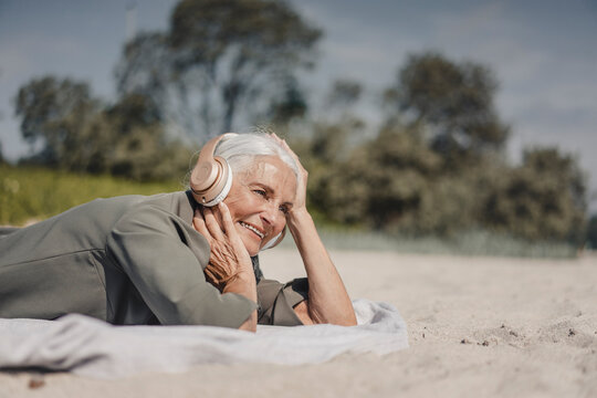 Senior woman listening music with headphones on the beach